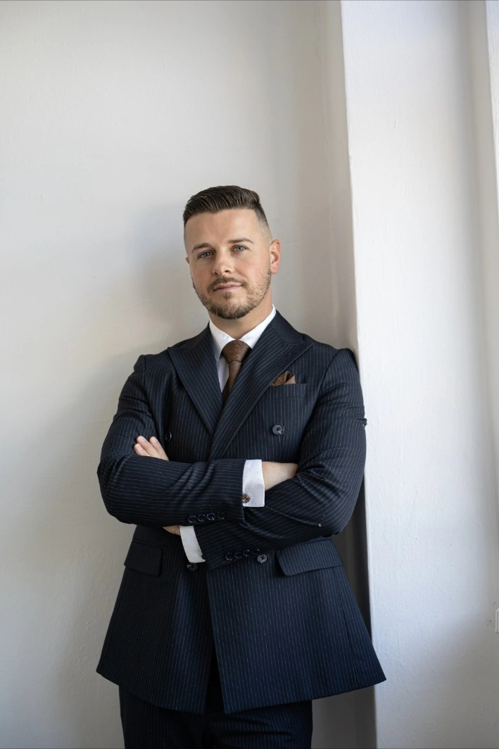 Király Dominik keresztbe tett karral, sötétkék öltönyben – a feltöltött teljes portré